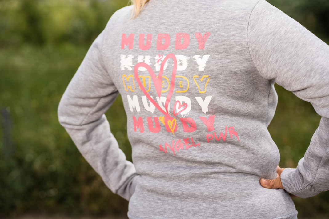 Rückseite einer Frau im Muddy-Angel-Sweater mit buntem „MUDDY“-Design, Herz und „ANGEL PWR“.