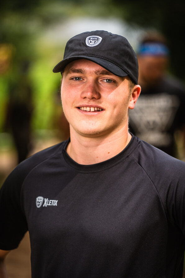Schwarze XLETIX-Cap kombiniert mit schwarzem T-Shirt, das links auf der Brust ein kleines XLETIX - Logo zeigt.