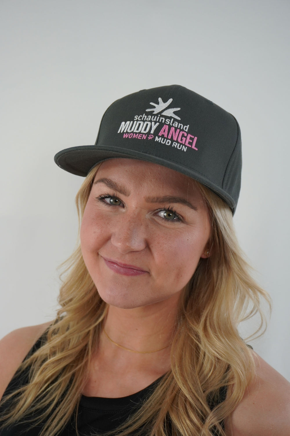 Frau mit langen blonden Haaren trägt eine dunkelgraue Muddy Angel Cap mit gesticktem Logo auf der Vorderseite.